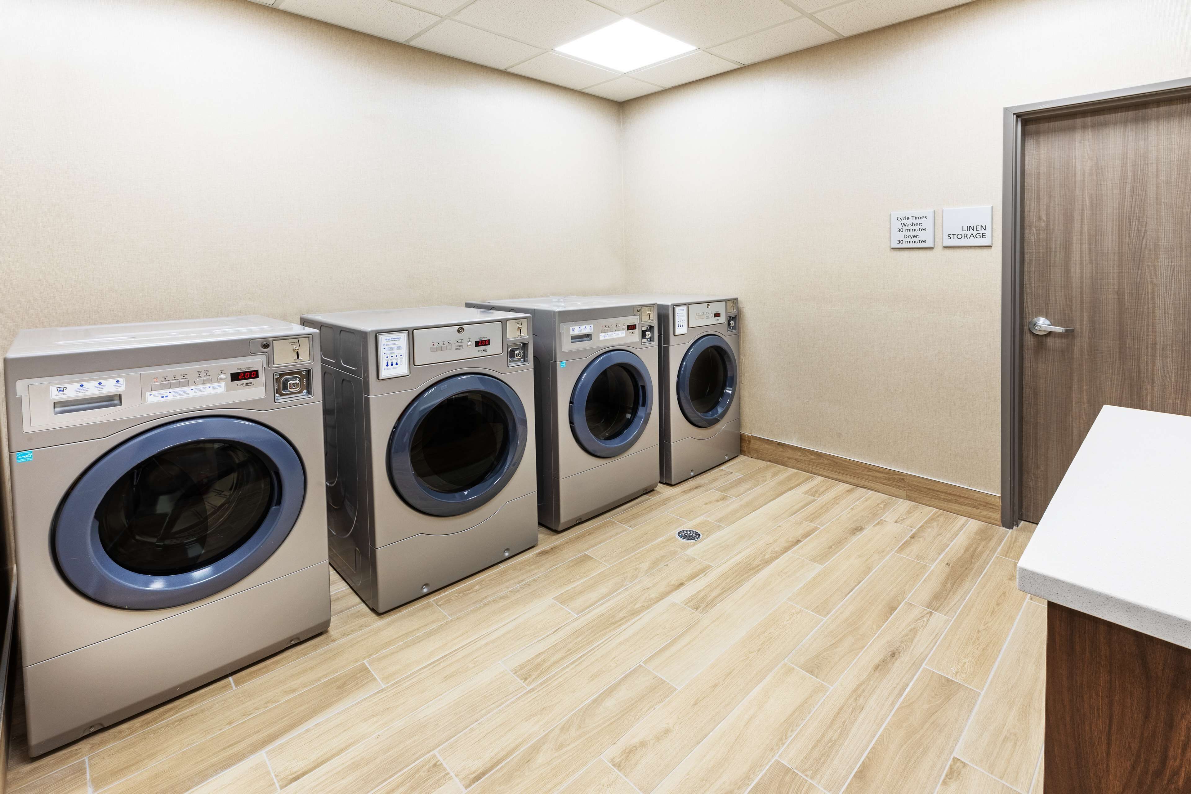 A laundry room with four front-loading washing machines, a linen storage sign, and a door.