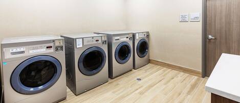 A laundry room with four front-loading washing machines, a linen storage sign, and a door.
