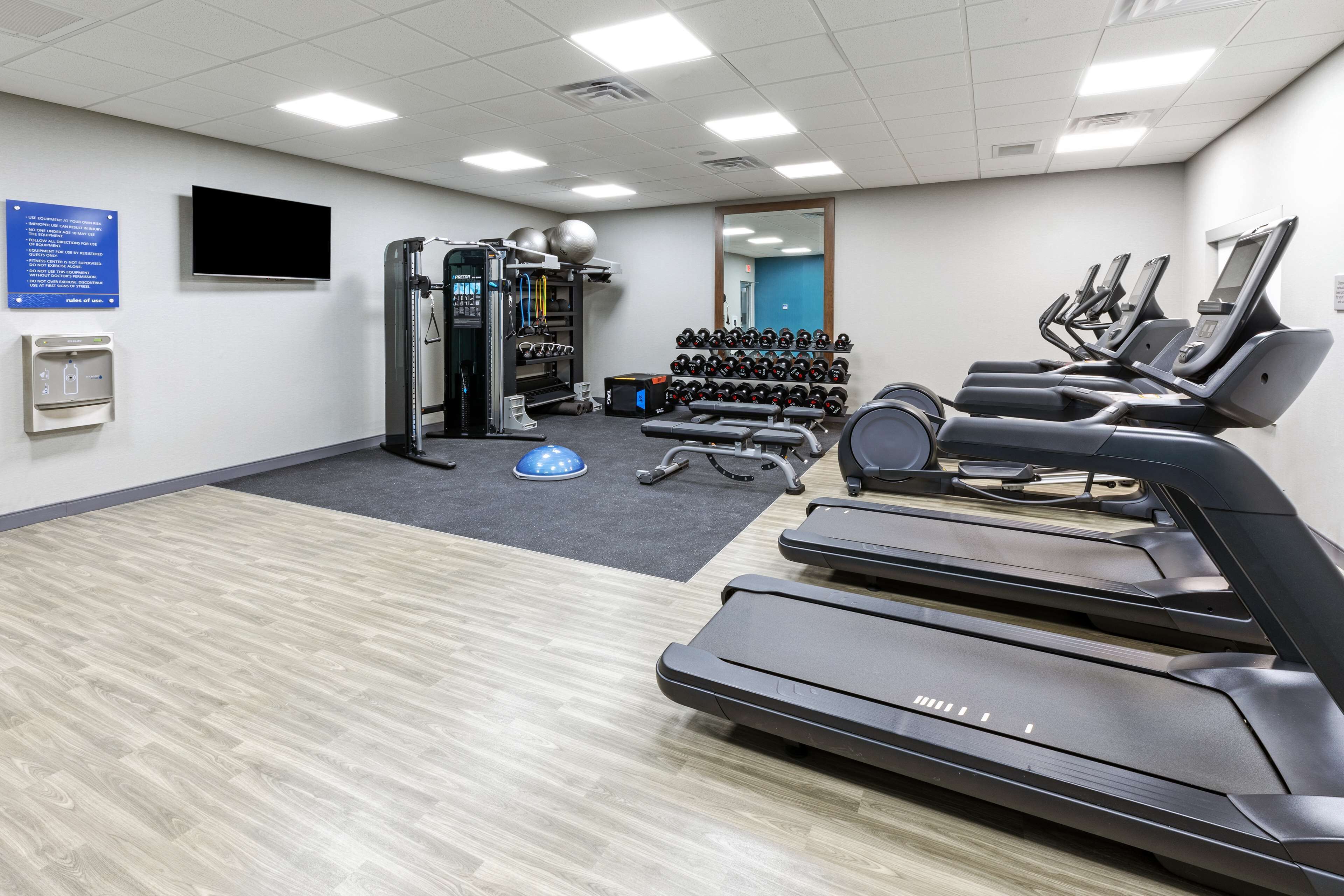 Un gimnasio con cintas de correr, máquinas de pesas y un televisor montado en la pared.