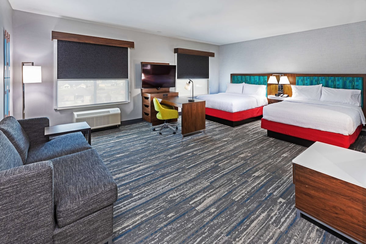 A hotel room with a large bed, a desk, a chair, and a sofa.