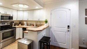 Cozinha moderna com armários brancos, eletrodomésticos de aço inoxidável, bancada de madeira e porta branca.
