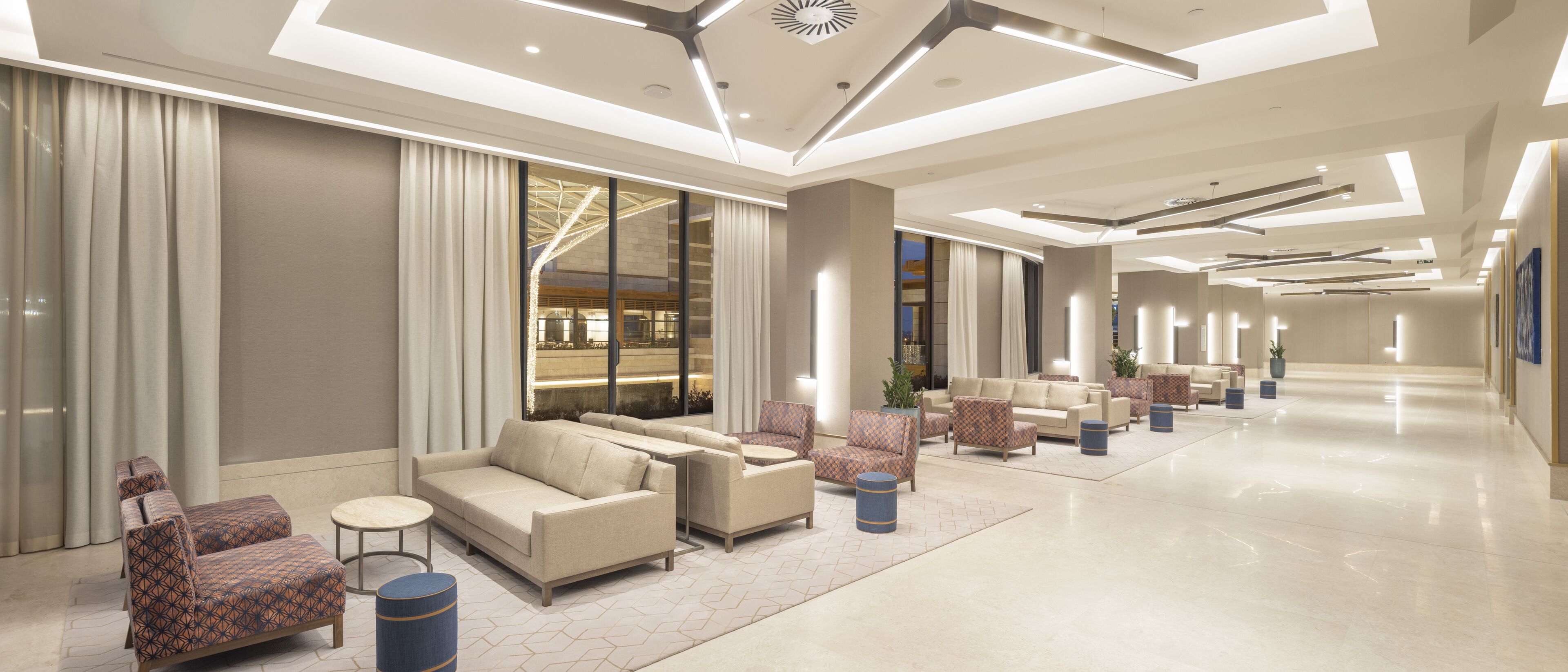 Eine geräumige Lobby mit modernem Design, inklusive einer langen Korridor mit Sitzbereichen und einem großen Fenster mit Blick nach außen.
