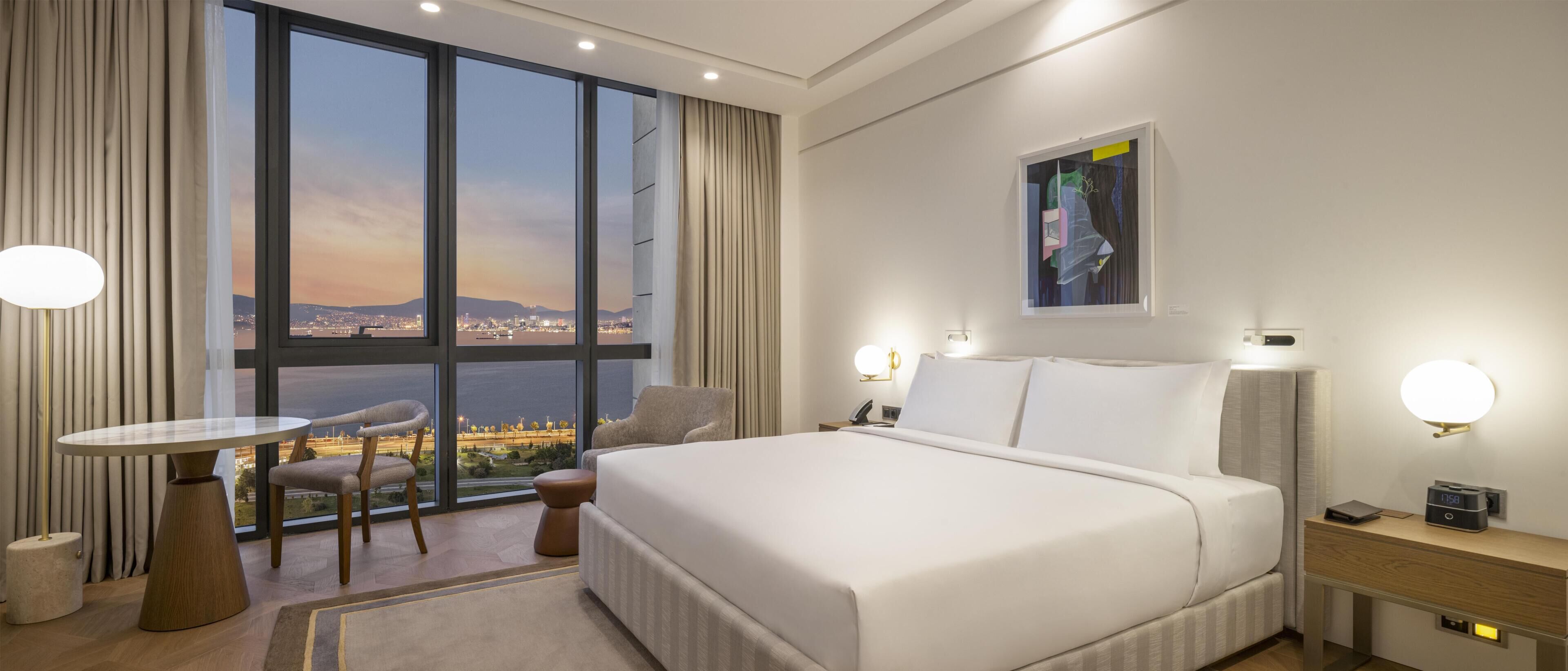 Habitación de hotel con una cama grande, un escritorio, una silla, vistas a la ciudad y un cuadro en la pared.