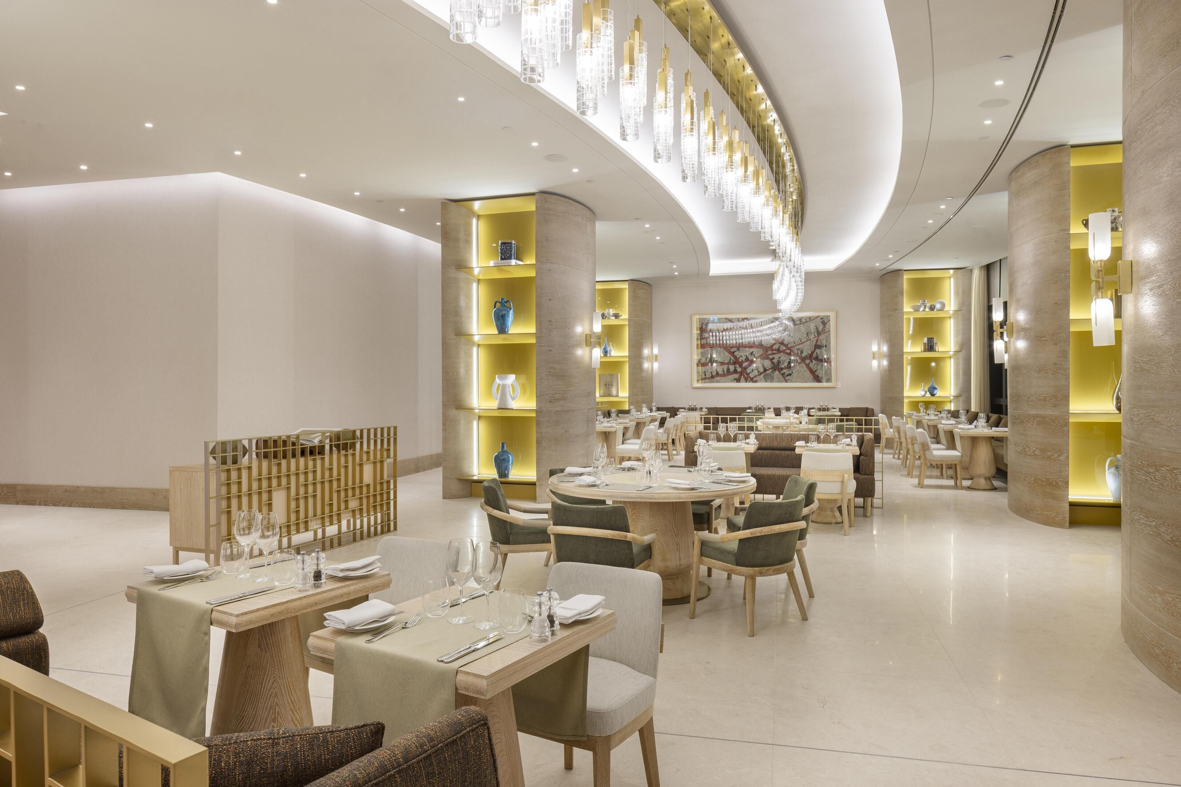 A modern dining area with round tables, chairs, and a central light fixture.