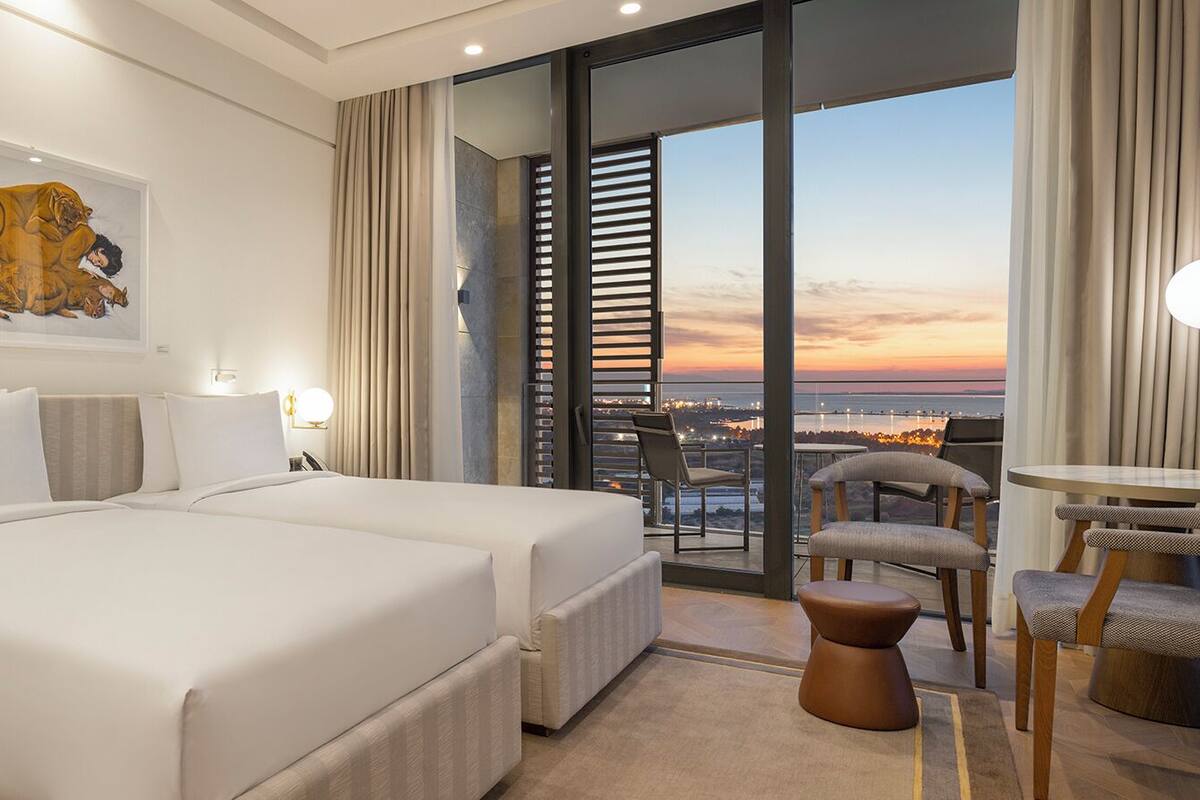 Een hotelkamer met een groot bed, een bureau met lamp, een stoel en uitzicht op de stadslijn.