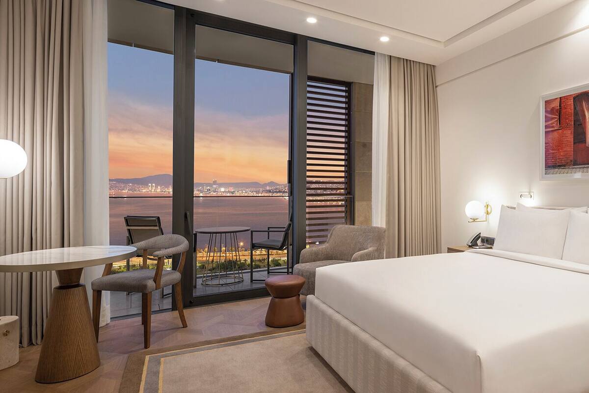 Een hotelkamer met een groot bed, een bureau, een stoel, uitzicht op de stad en een schilderij aan de muur.