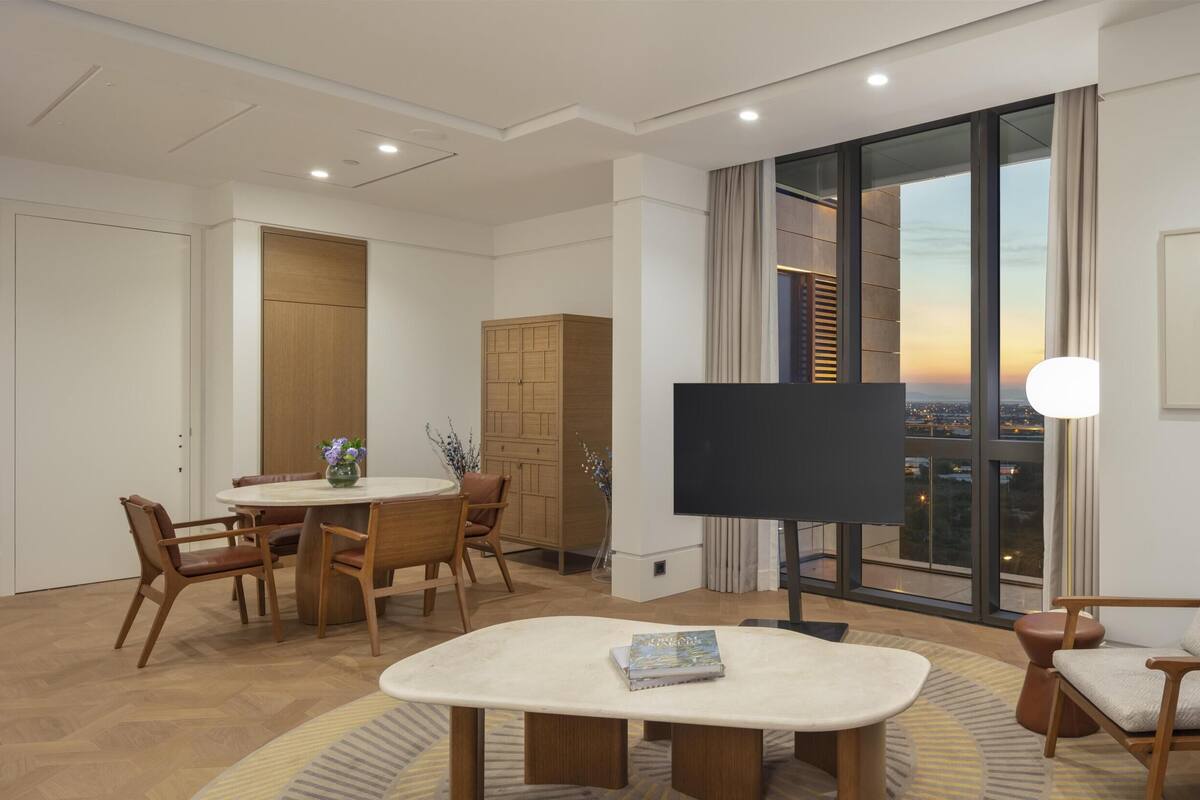 Een moderne hotelkamer met een zithoek, een flatscreen televisie, een groot raam met uitzicht over de stad en een lijst met een afbeelding aan de muur.