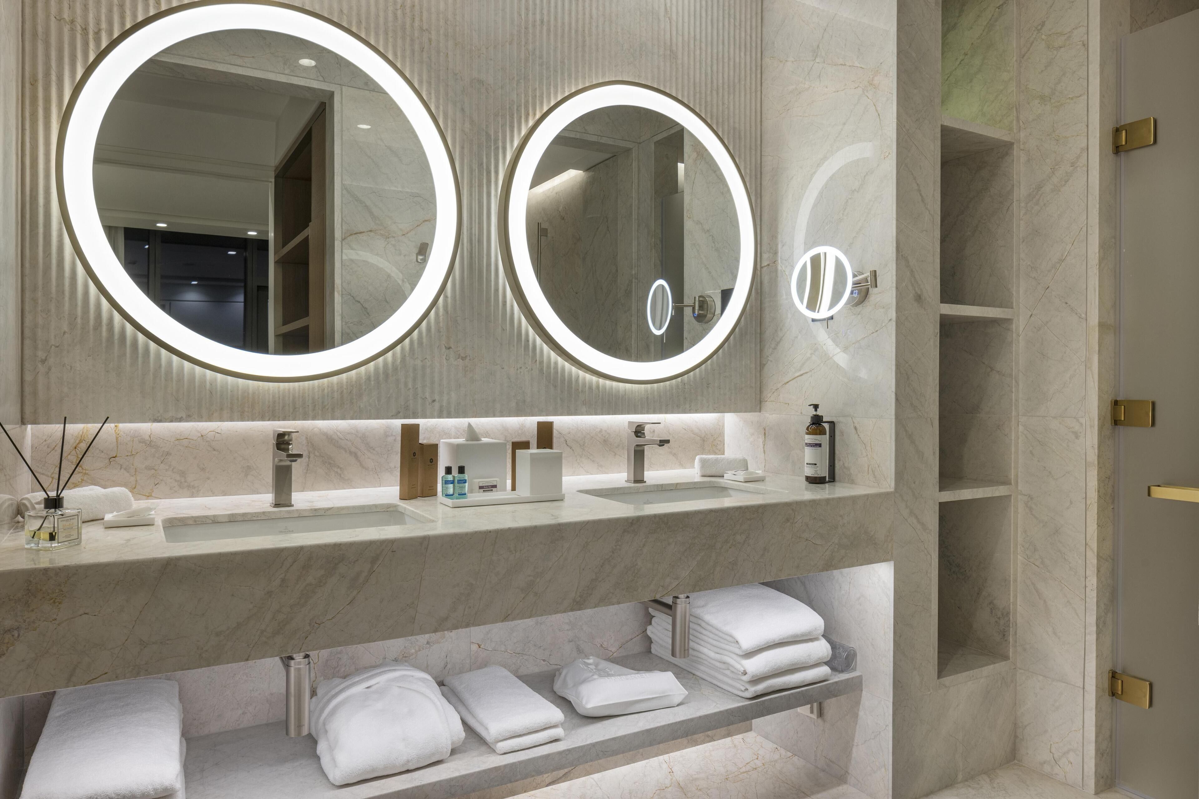 Un baño con dos espejos redondos, un lavamanos y un estante con toallas.