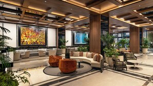 A spacious lobby with a modern design, featuring a seating area with sofas and chairs, a large abstract painting, and potted plants.