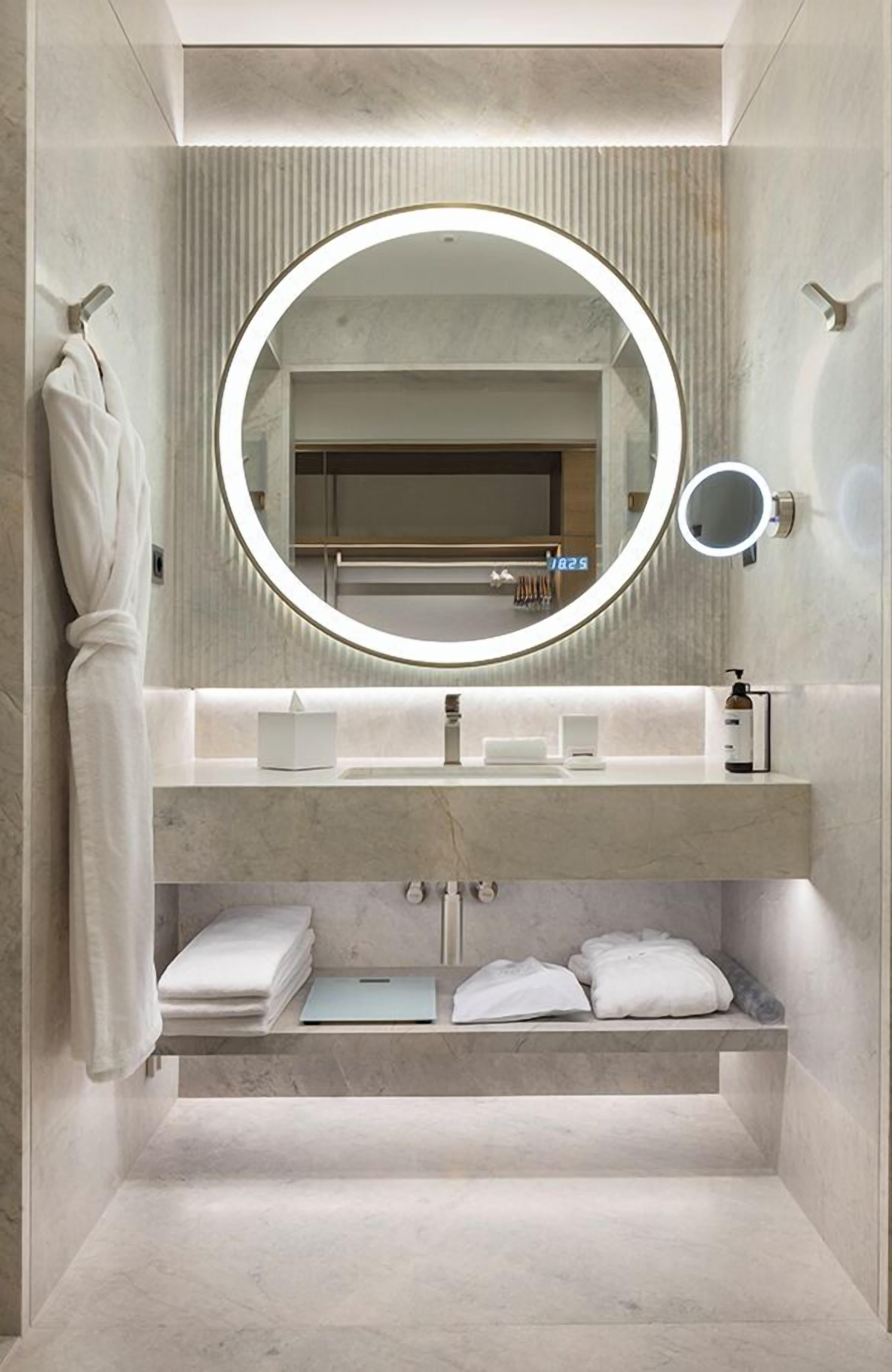 A modern bathroom with a large mirror, a towel rack, a vanity with a sink, and a built-in shelf for towels.