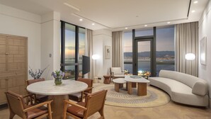 A modern living room with a round dining table, a sofa, and a view of a cityscape through large windows.