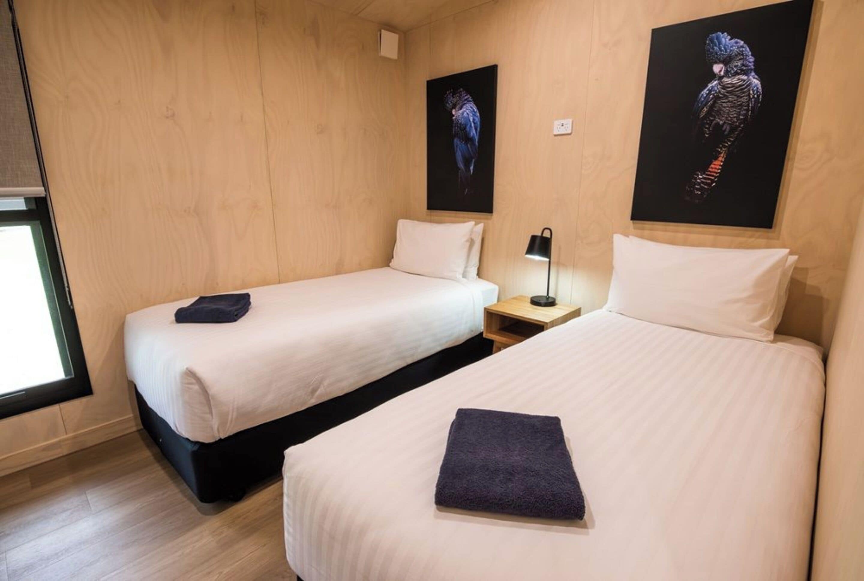 A hotel room with two beds, wooden walls, and artwork on the walls.