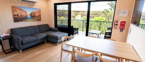 Una habitación con sofá, mesa y sillas, un balcón con vistas y un extintor de incendios en la pared.