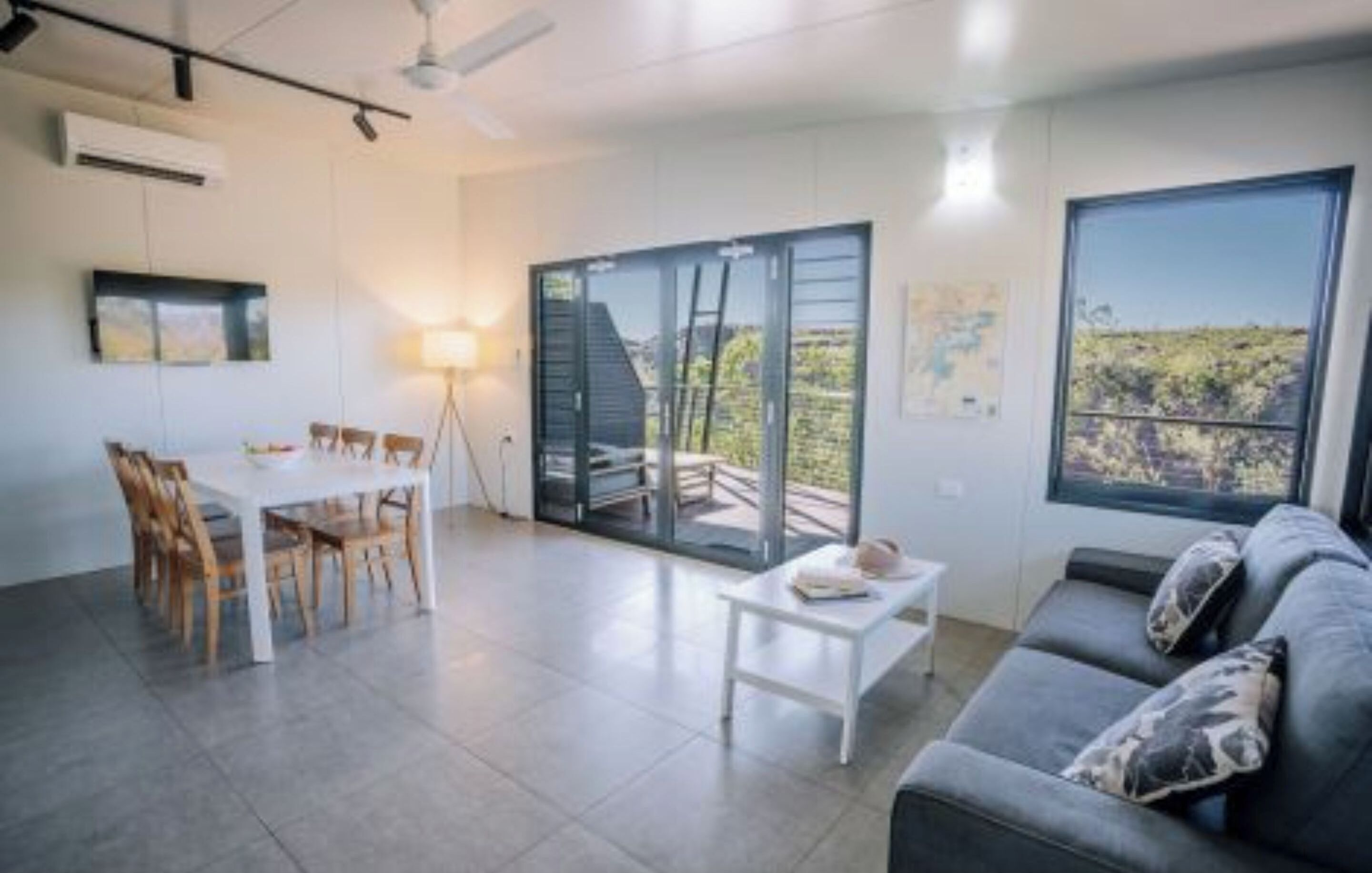 A modern living room with a dining area, a sofa, and a large window offering a view of the outdoors.