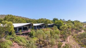 A series of modern, single-story buildings with flat roofs, surrounded by dense shrubbery and trees, set on a hillside. - Discovery Resorts- Lake Argyle (Lake Argyle)