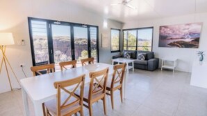 A spacious living area with a dining table and chairs, a sofa, and large windows offering a view of the landscape. - Discovery Resorts- Lake Argyle (Lake Argyle)