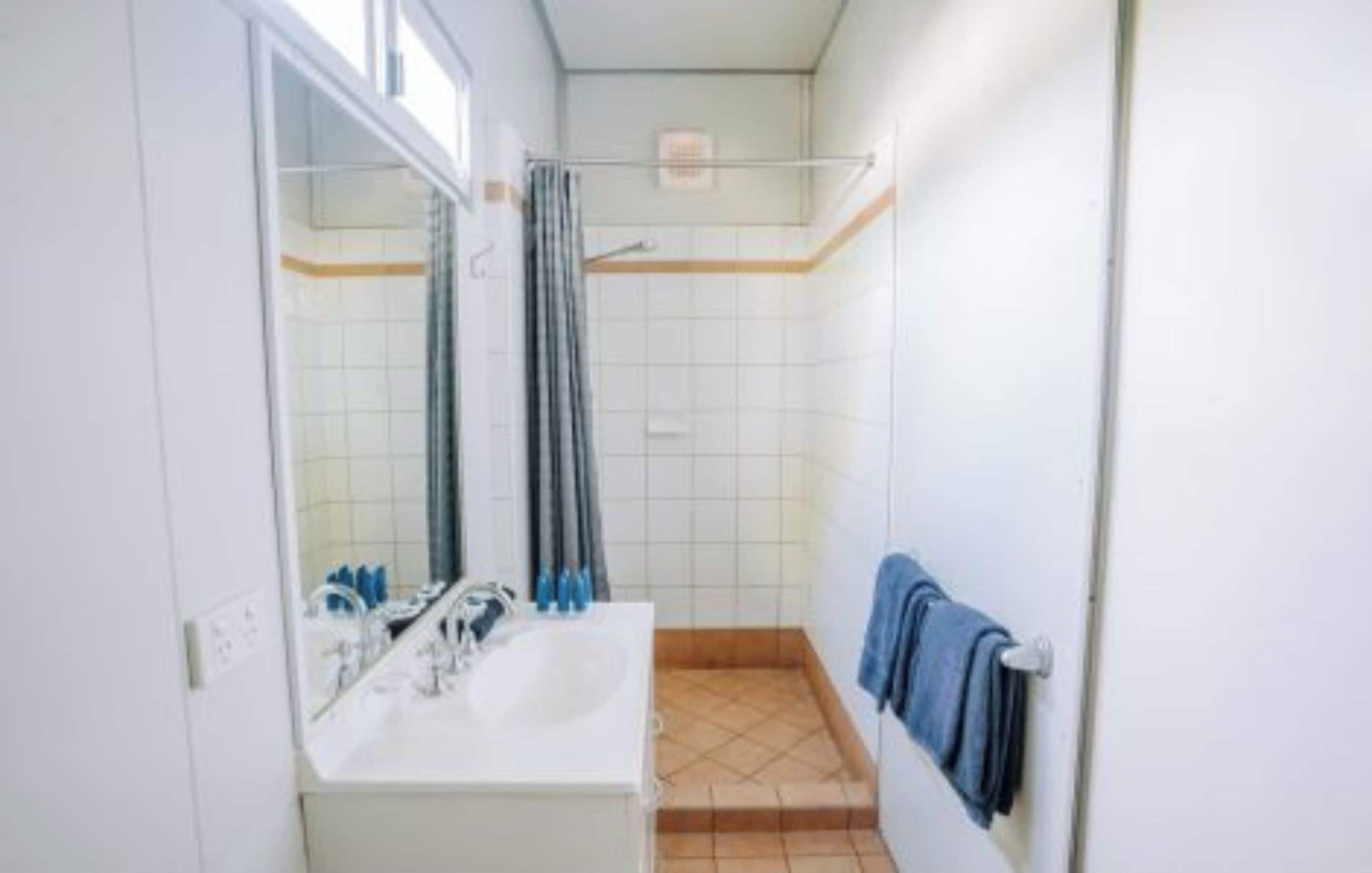 Een badkamer met een wastafel, spiegel, douche en handdoekrek.