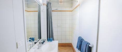 A bathroom with a sink, mirror, shower, and towel rack.