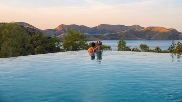 A couple relaxing in a clear infinity pool with a view of mountains and trees. - Discovery Resorts- Lake Argyle (Lake Argyle)