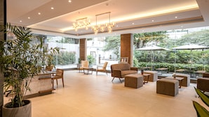 A spacious lobby with modern furniture, large windows offering views of greenery, and a stylish chandelier. - The Sulit Whitefield (Bengaluru)