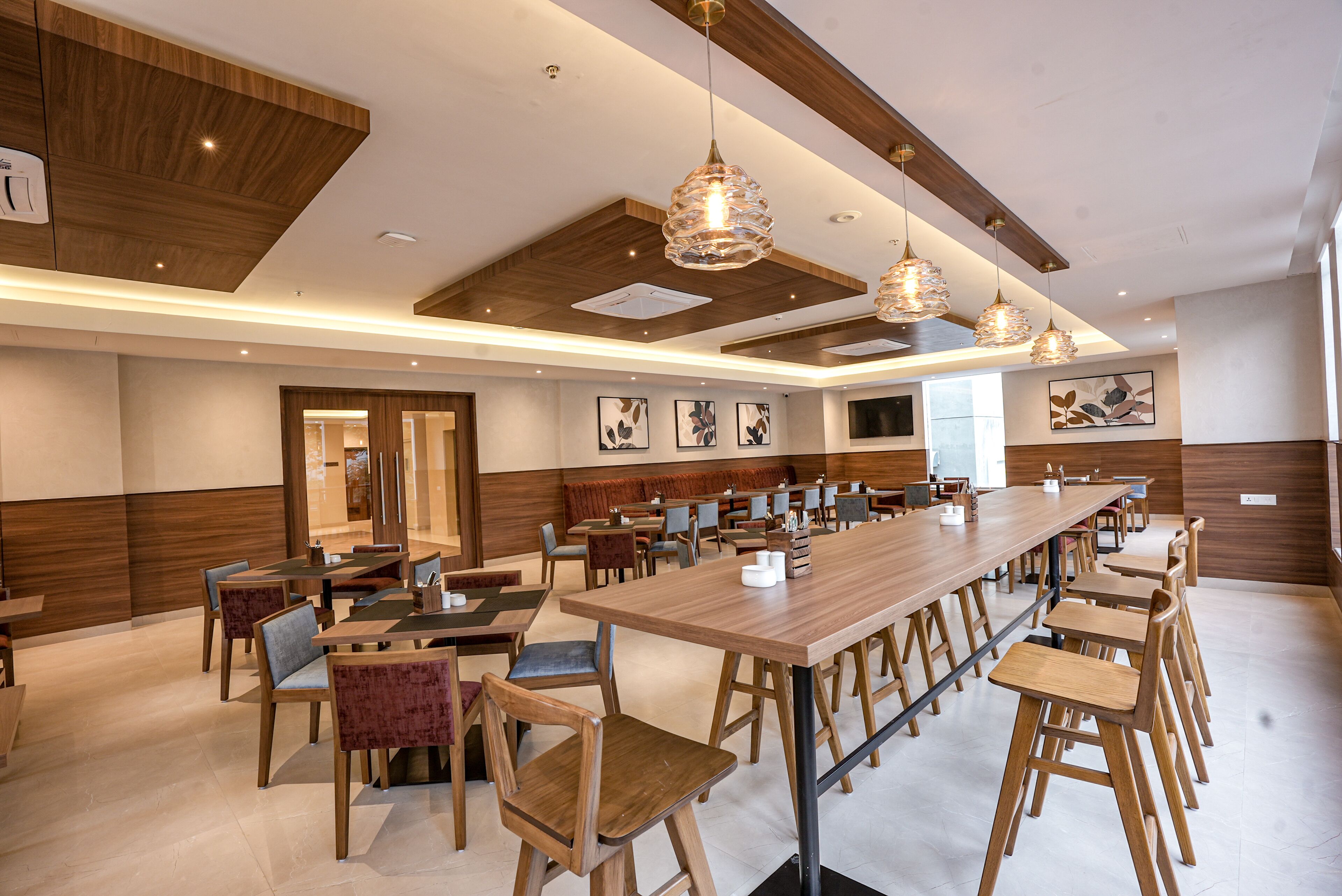 Un amplio comedor con largas mesas y sillas de madera, iluminación colgante y obras de arte en las paredes.