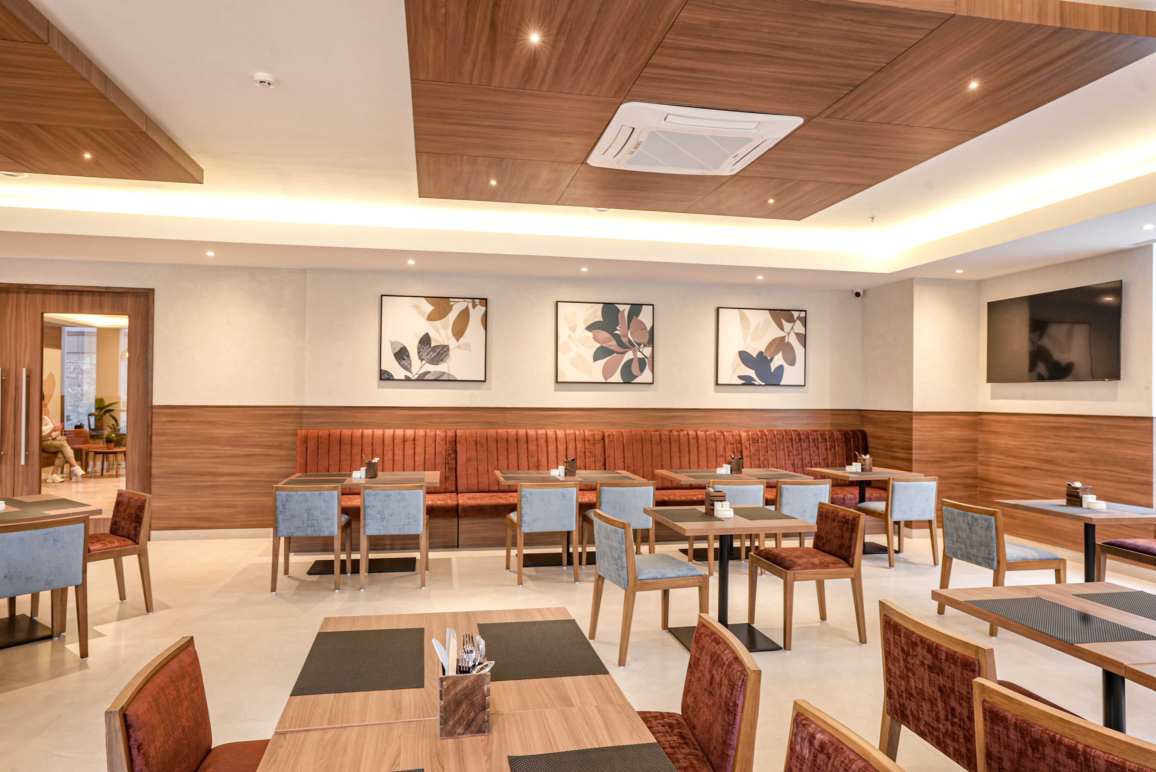 Un restaurante moderno con techos de paneles de madera, un área central de asientos con bancos acolchados y múltiples mesas de comedor con sillas.