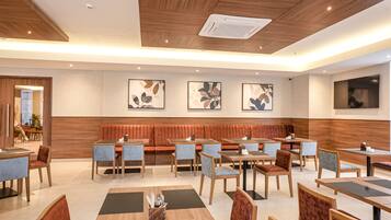 Un restaurante moderno con techos de paneles de madera, un área central de asientos con bancos acolchados y múltiples mesas de comedor con sillas.