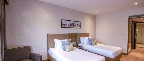 A hotel room with two beds, a sofa, a small table with a newspaper, and a painting on the wall.