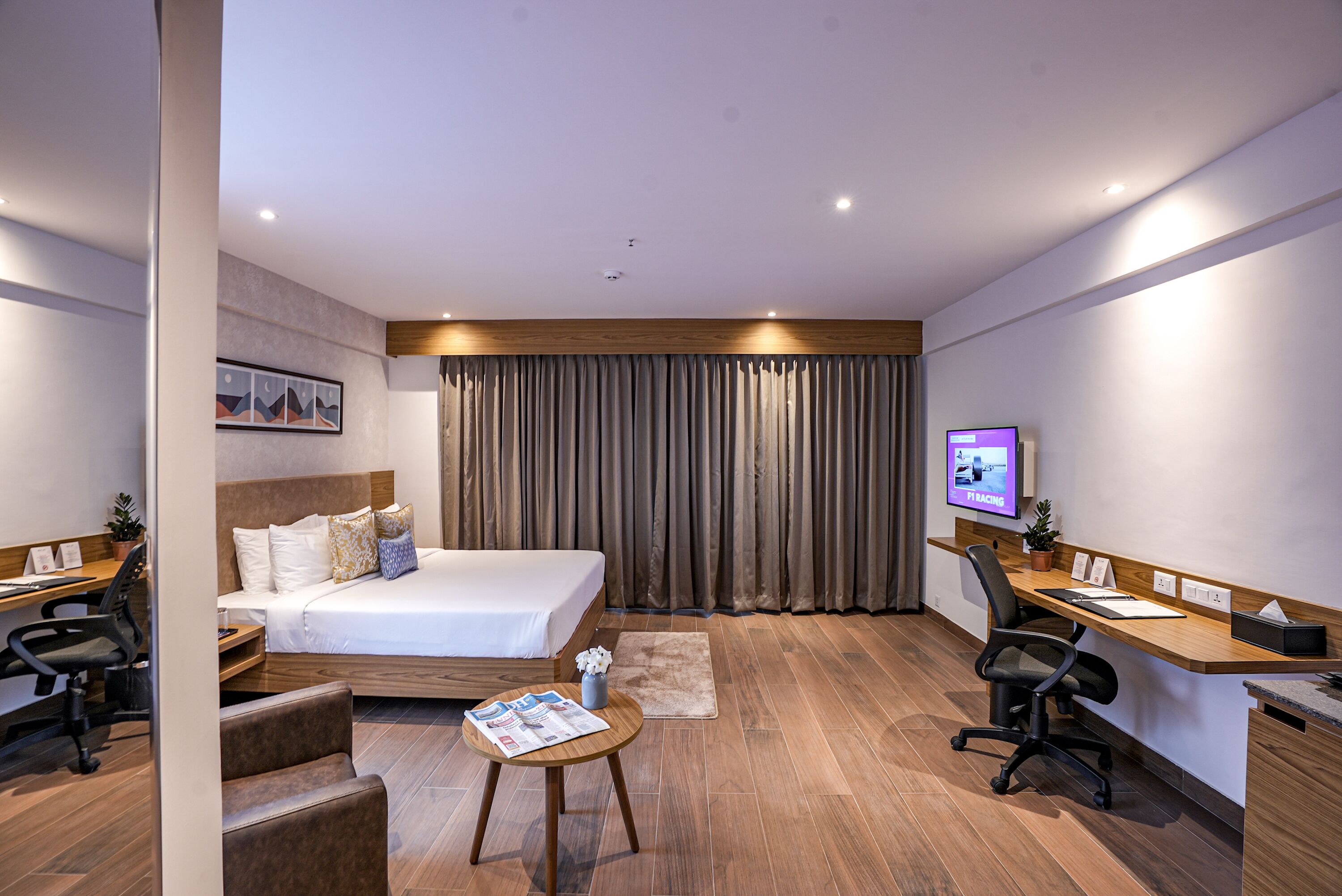 Una habitación de hotel moderna con una cama grande, dos escritorios, una silla y un televisor.