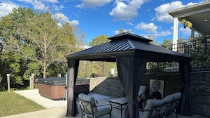 An outdoor patio with a gazebo, seating, and a hot tub.