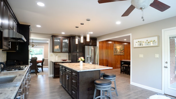 A modern kitchen with dark cabinets, a large island, pendant lights, and a ceiling fan.