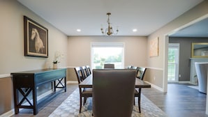 A dining area with a long table, chairs, a bench, and a chandelier.