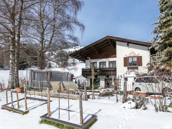 A two-story chalet with a wooden balcony, a white exterior, and a snow-covered landscape.