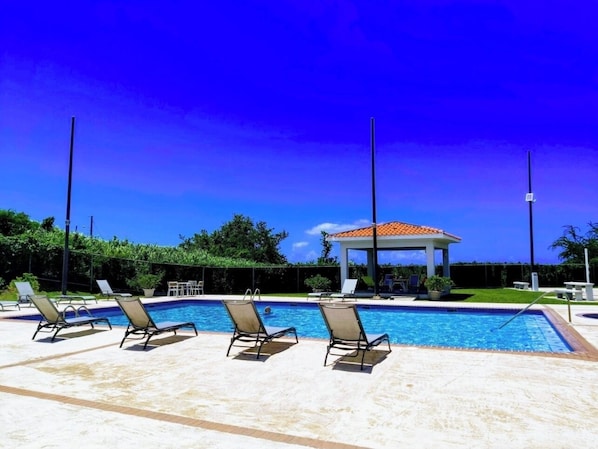 Una piscina con sillones de descanso y un pabellón.