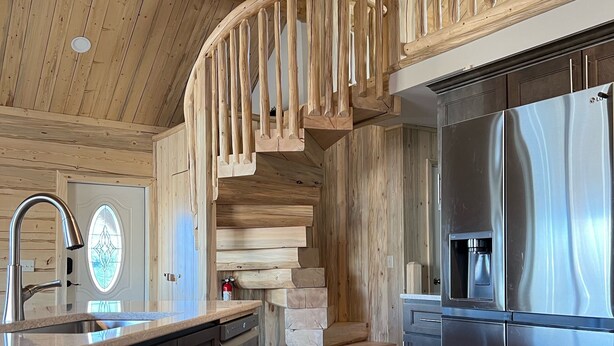 A modern kitchen with wooden accents, a stainless steel refrigerator, and a wooden staircase. - Beautiful hand-crafted log cabin on Horse Creek one block off Main Street. (Dubois)