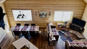 A cozy cabin interior with a dining area, sofa, TV, and a wooden ceiling. - Beautiful hand-crafted log cabin on Horse Creek one block off Main Street. (Dubois)