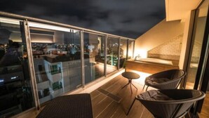 A modern balcony with glass doors, a wooden floor, and two wicker chairs. - Hotel Brick (Naha)