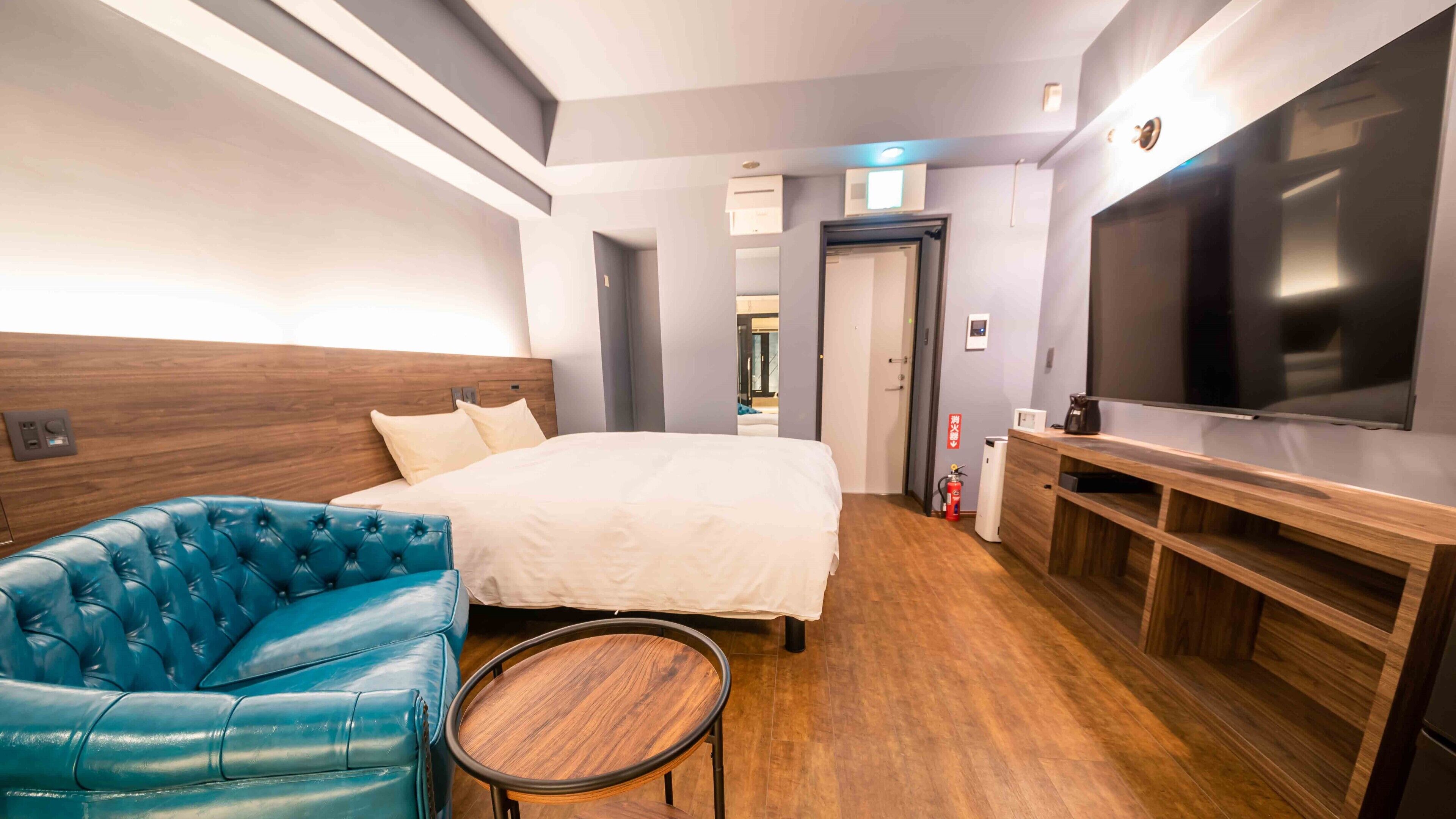 A hotel room with a bed, a blue leather sofa, a small wooden table, a TV, and a minibar.