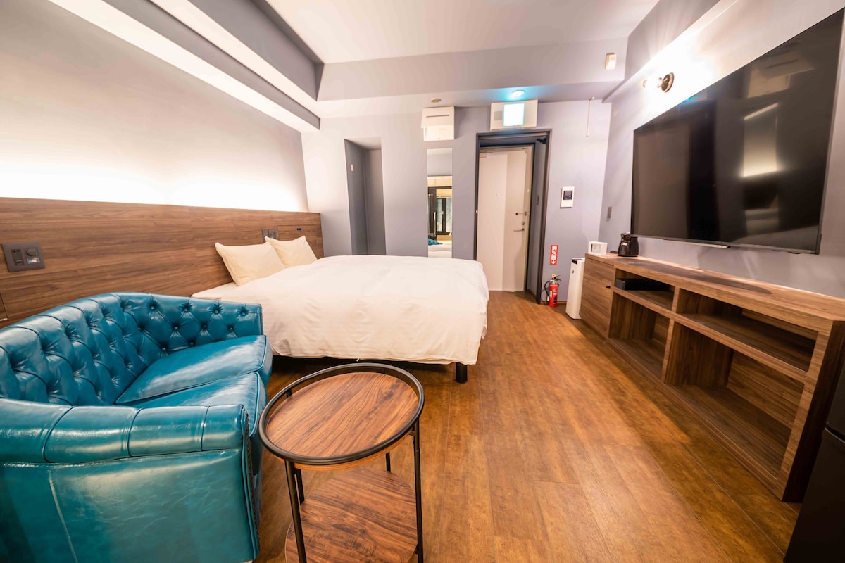 A hotel room with a large bed, a blue leather sofa, a small wooden table, a TV, and a wooden TV stand.