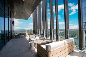 Une terrasse extérieure moderne, offrant une vue sur un plan d’eau et des bâtiments, et aménagée avec des sièges et des tables.