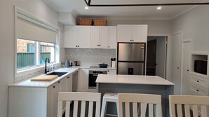 Une cuisine moderne avec des meubles blancs, un réfrigérateur en acier inoxydable et un coin repas avec des chaises blanches.