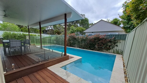 Un jardin avec une piscine, une terrasse en bois et du mobilier d’extérieur.