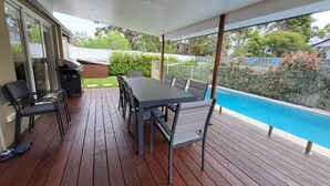 Un espace extérieur abrité doté d’une terrasse en bois, d’une table avec des chaises et d’une vue sur une piscine.
