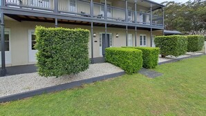 Un bâtiment à deux étages doté d’un balcon, d’une pelouse bien entretenue et de haies soigneusement taillées.