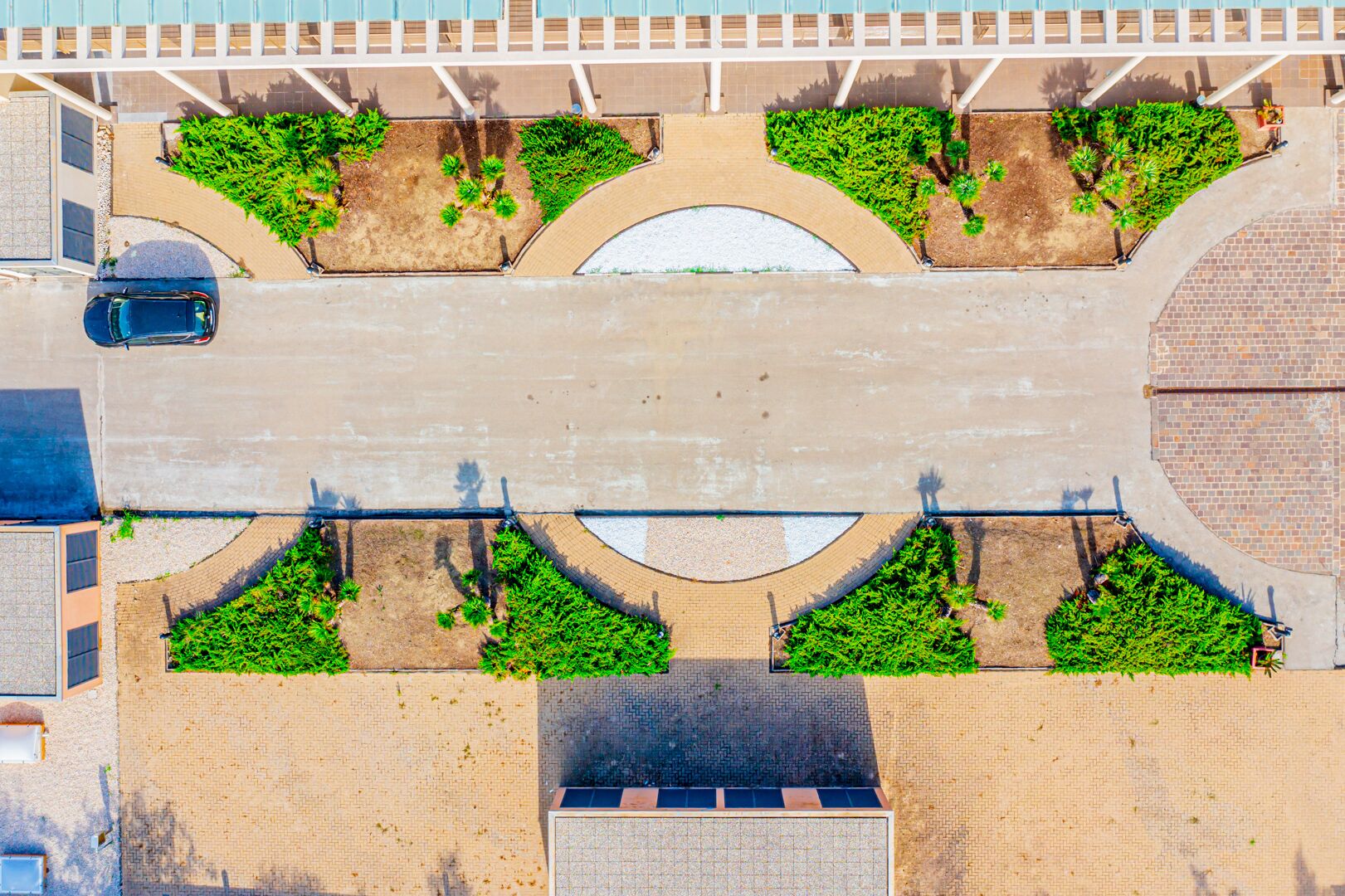 An aerial view of a parking lot with multiple green landscaped areas and a central paved road.