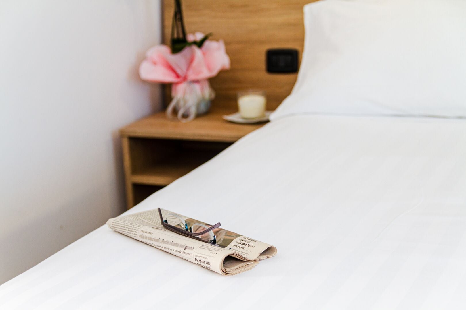 Una cama bien tendida con un periódico y un par de gafas encima.