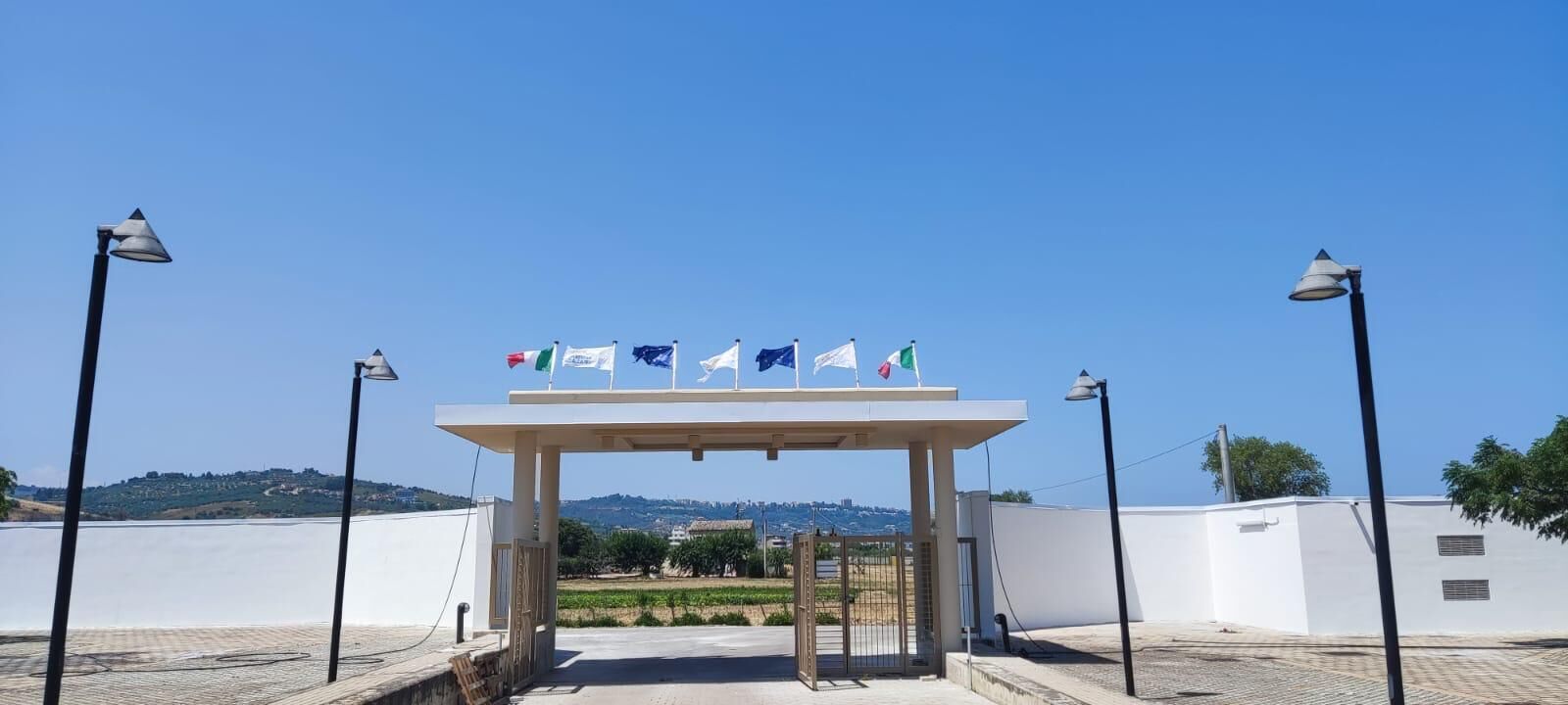A covered entrance with flags, a clear sky, and a view of a hilly landscape.