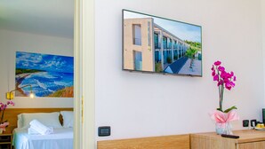 A hotel room with a bed, a desk, a chair, a small table with a vase of flowers, and a painting of a building on the wall. - Residence al Palace (Vasto)