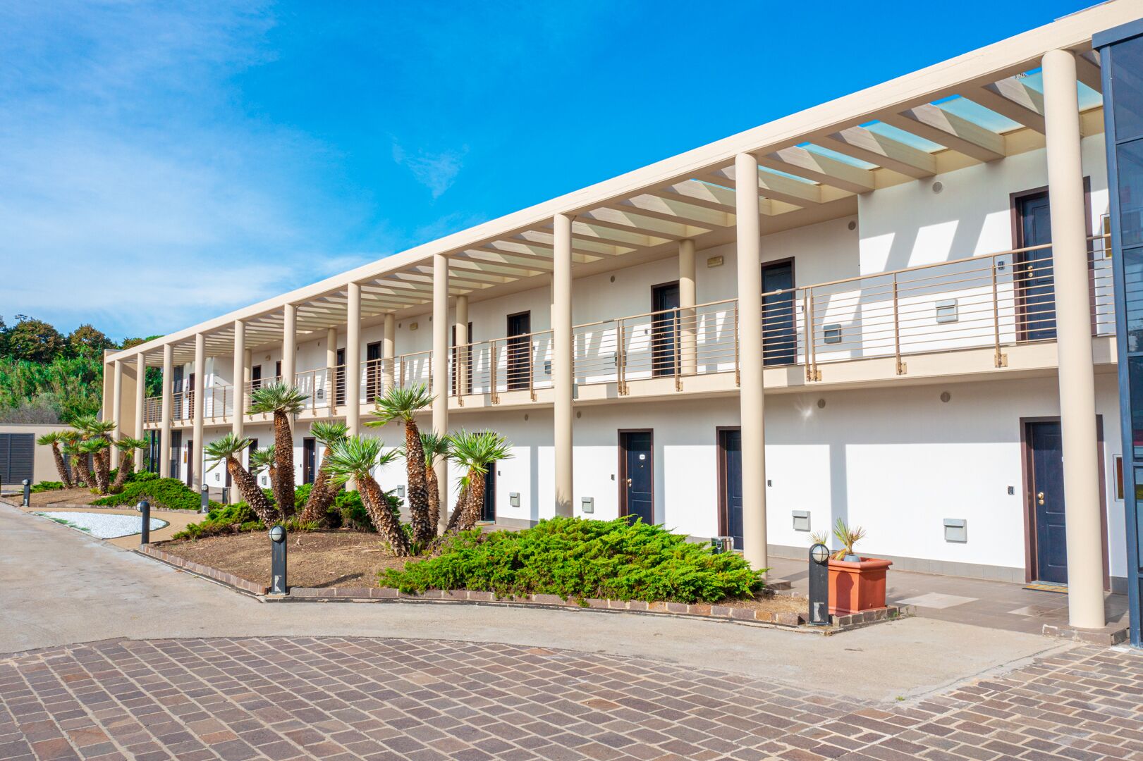 A modern building with a covered walkway, multiple balconies, and palm trees.
