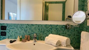 Ein Badezimmer mit einem weißen Waschbecken, grünen Fliesen und einem Spiegel, sowie einem Handtuch.